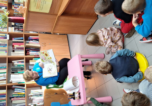Dzieci słuchają opowiadania czytanego przez panią bibliotekarkę