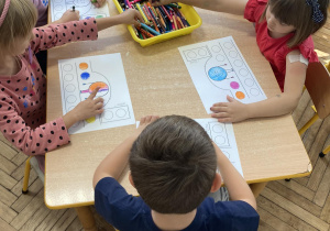 Dzieci siedzą przy stoliku i kolorują obrazek