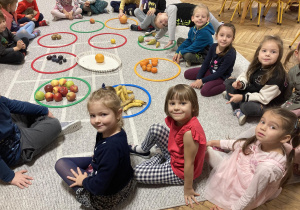 Dzieci siedzą na dywanie z posegregowanymi owocami