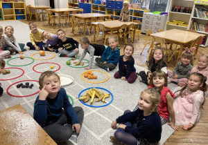 Dzieci siedzą na dywanie z posegregowanymi owocami