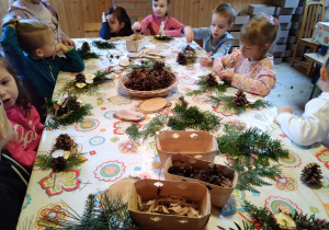 Dzieci siedzą przy stole i wykonują stroik świąteczny