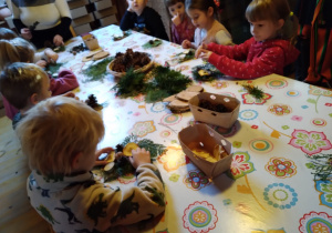 Dzieci siedzą przy stole i wykonują stroik świąteczny
